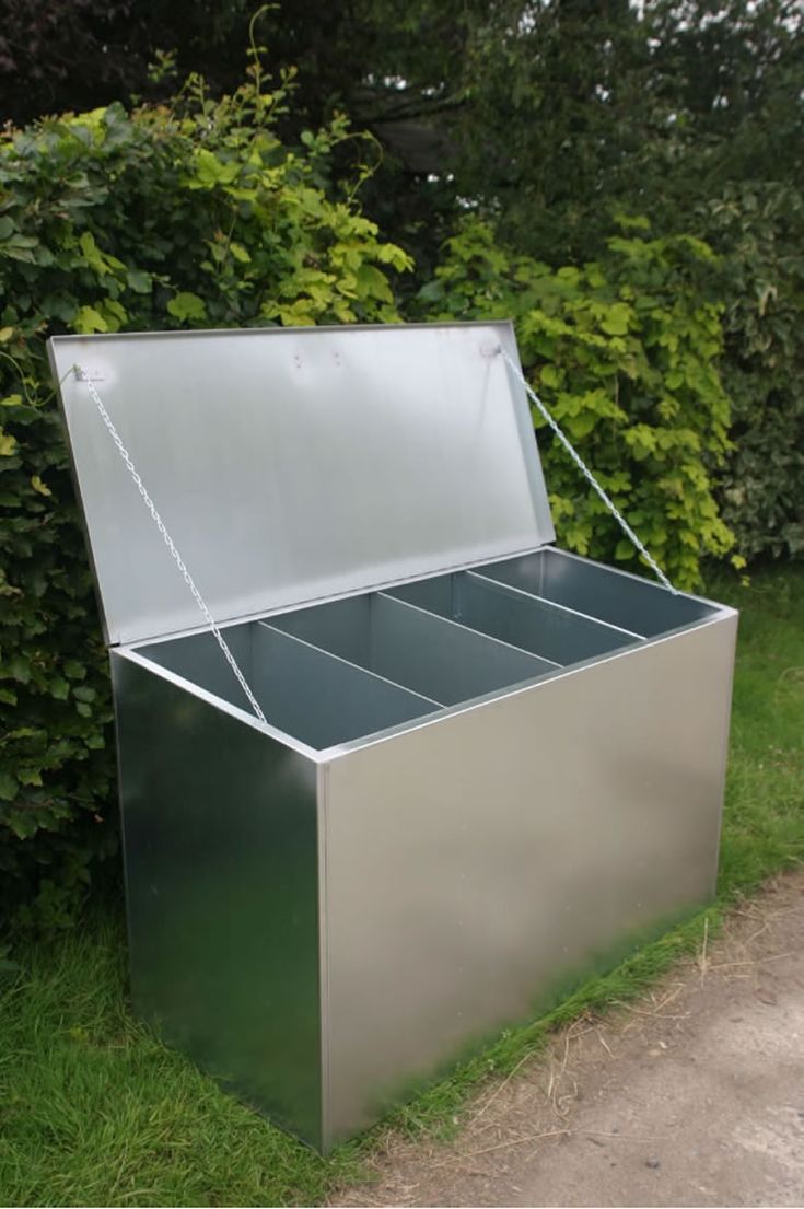 an open metal box sitting on the side of a road next to some grass and bushes