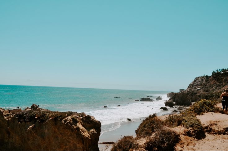 two people are walking along the beach near the ocean