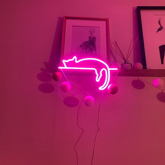 a pink neon sign with a cat on it's back hanging from a shelf