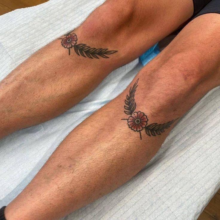 two people with tattoos on their legs sitting on a bed and one has a flower tattoo on his leg