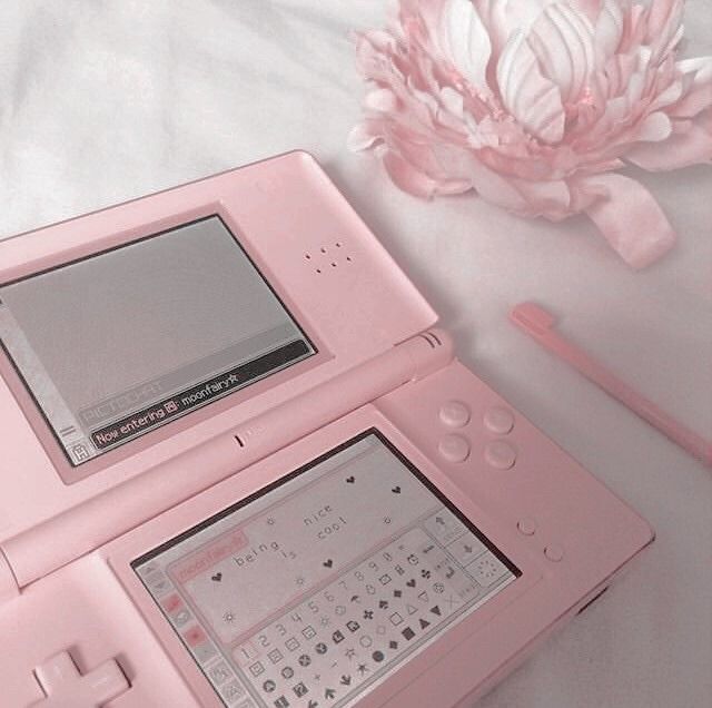 an electronic device sitting on top of a bed next to a pink flower and pen