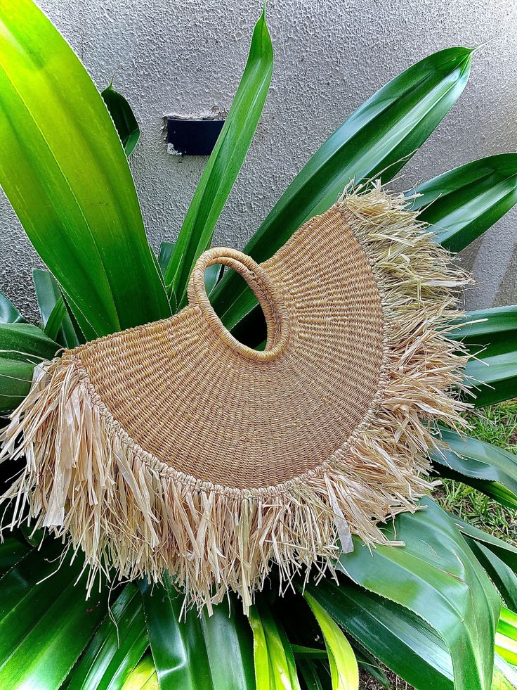 a straw bag sitting on top of some green leaves next to a building with a wall in the background