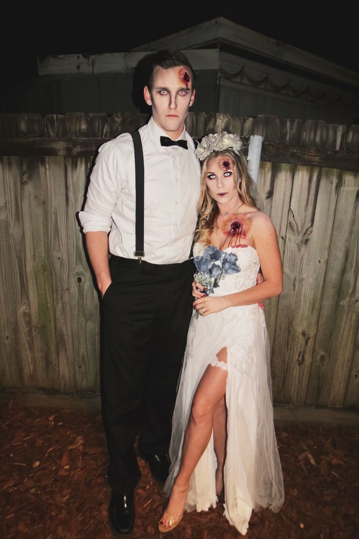 a man and woman dressed up as zombies for a halloween costume party in front of a wooden fence