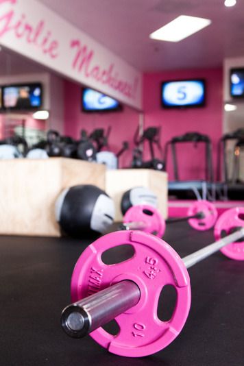 a pink barbell set up in a gym with tvs and exercise equipment behind it