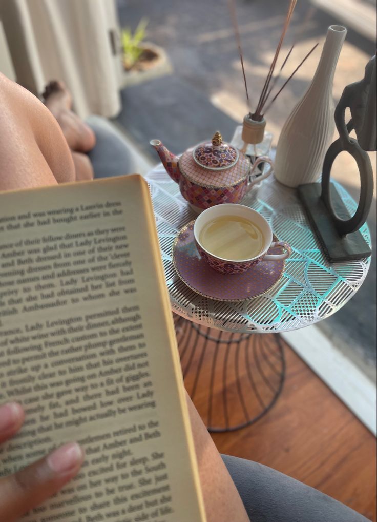 a person is reading a book with a cup of coffee in front of them on a table