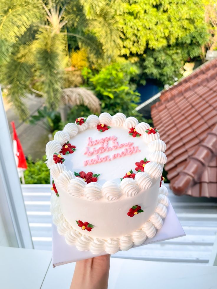 a person holding up a white frosted birthday cake