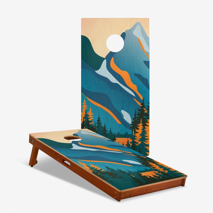 a cornhole game board with mountains and trees painted on the back side, as well as a hole in the middle