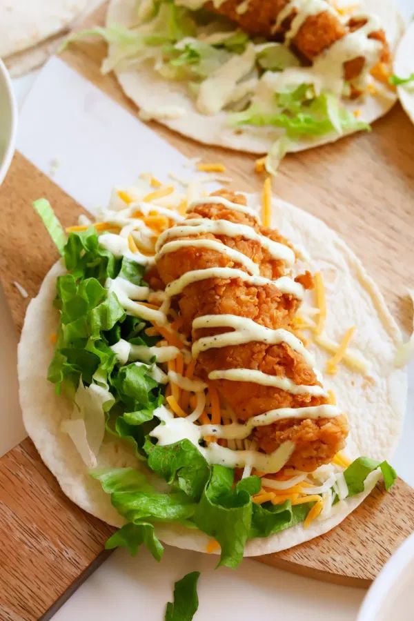 two tacos with chicken, lettuce and cheese on them sitting on a cutting board