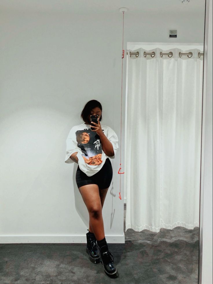 Black girl standing in front of mirror, posing in a white oversized space graphic kenzo t-shirt. Styled with black biker shorts and black dr martens boots. Biker Short And Graphic Tee Outfit, Oversized Shirt With Biker Shorts Outfit, Combat Boots And Shorts Outfit Black Women, Biker Shorts And Combat Boots, Graphic Tee And Shorts Black Women, Biker Shorts Boots Outfit, Boots With Shorts Outfit Summer, Shorts With Docs Outfits, Shorts And Boots Outfits Summer