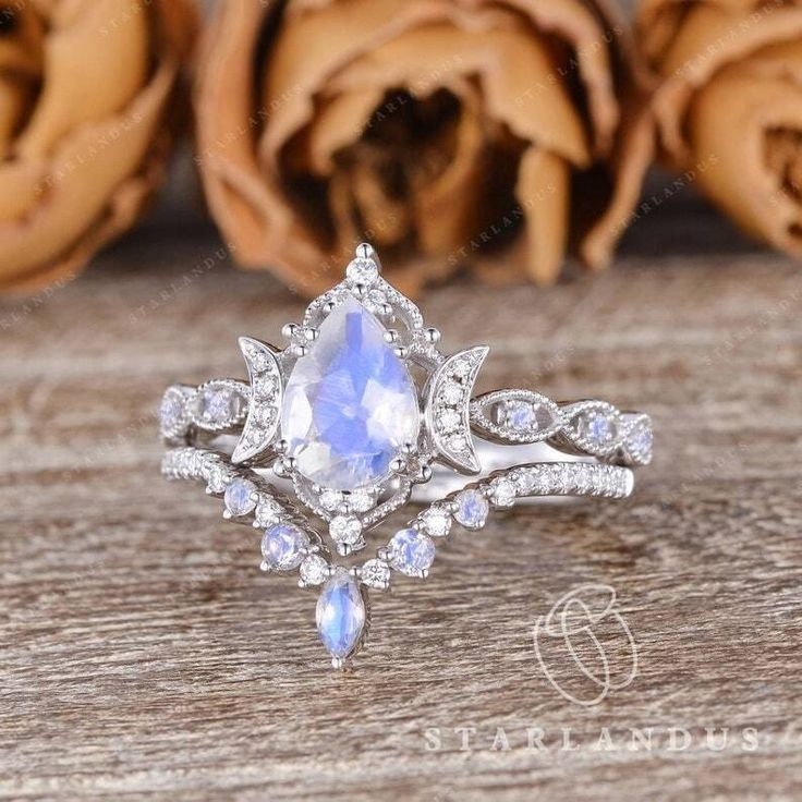 an engagement ring with a pear shaped blue and white stone surrounded by diamonds on a wooden surface