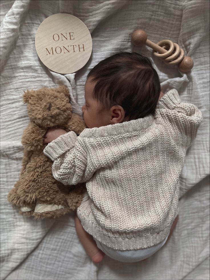 a baby sleeping next to a teddy bear with a one month sign on it's back