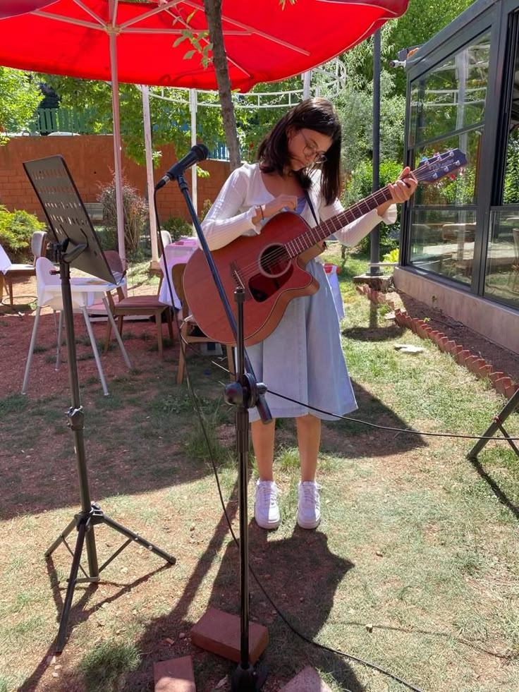 a woman standing in front of a microphone and holding a guitar on top of a field