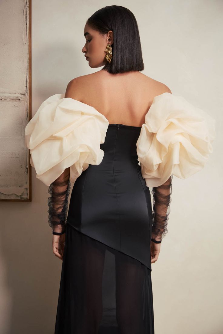 the back of a woman wearing a black dress with sheer sleeves and an open shoulder