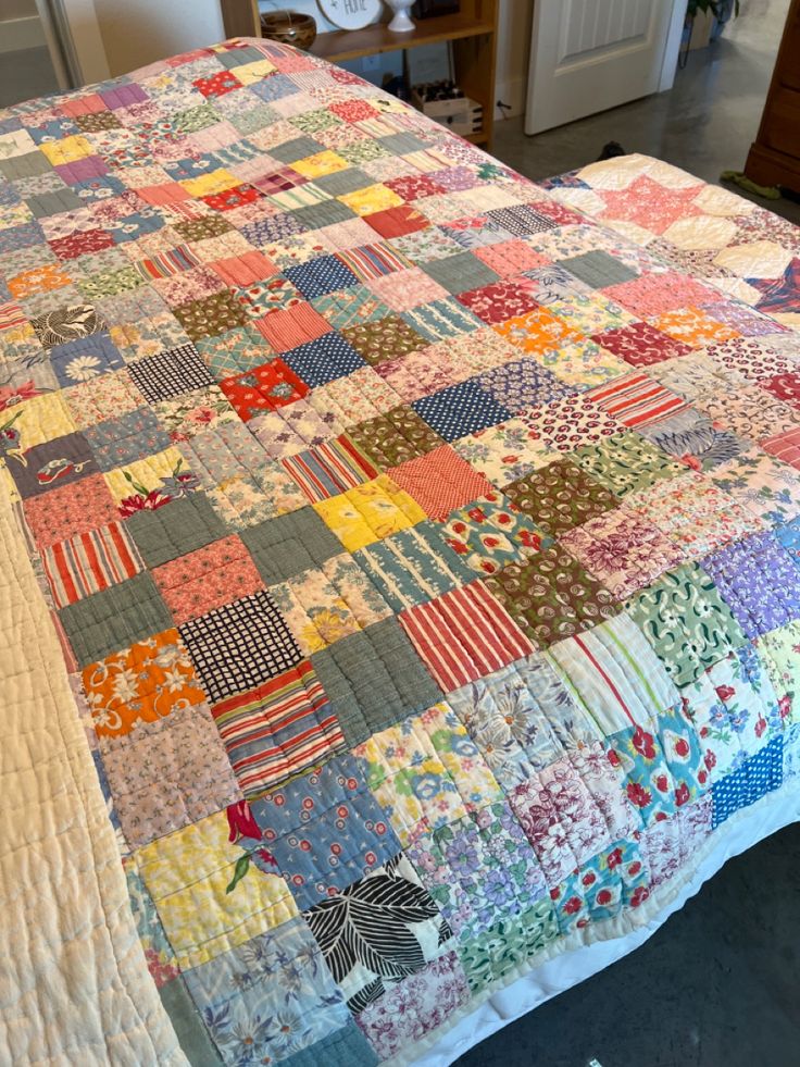 a bed with a quilt on top of it in a room next to a dresser