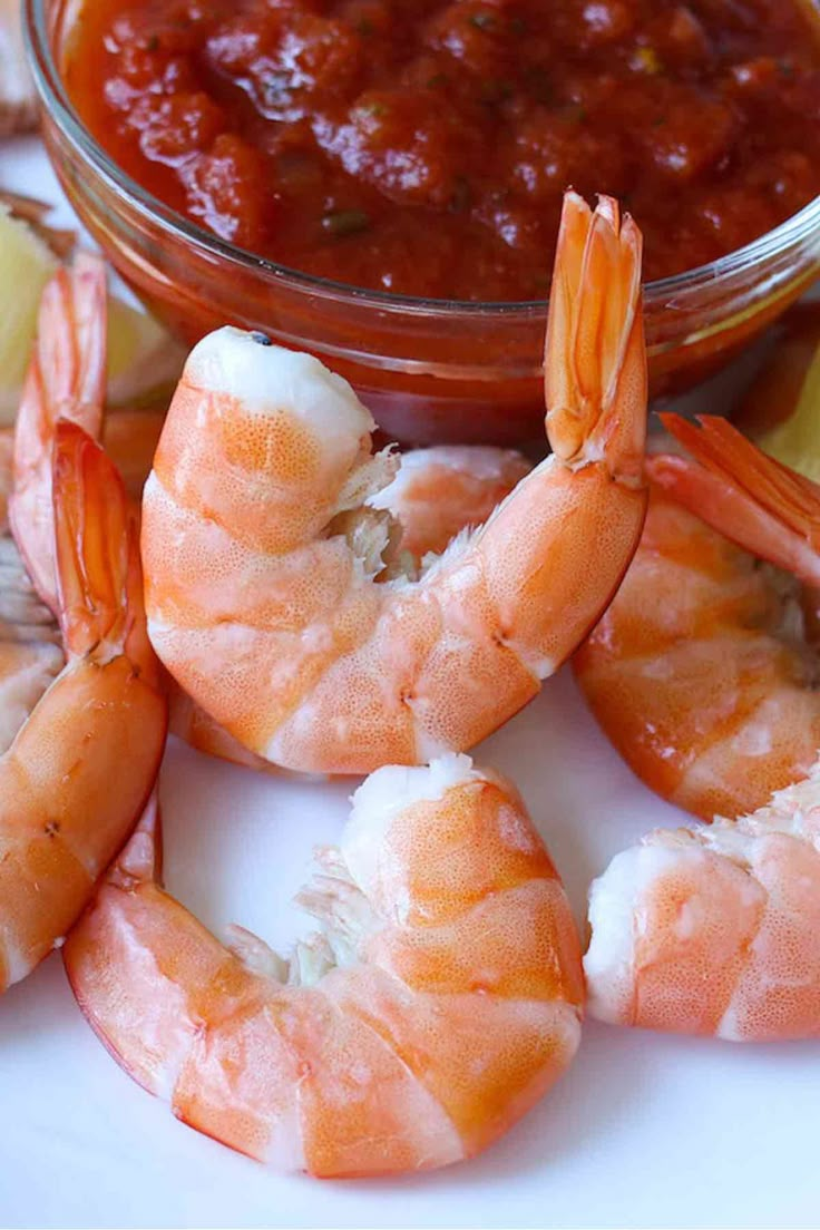 some shrimp are on a white plate with lemon wedges and ketchup in a bowl