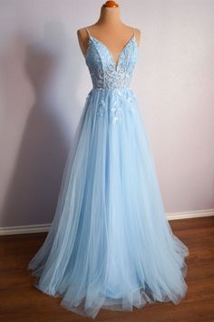 a light blue prom dress on display in front of a white wall and wooden floor