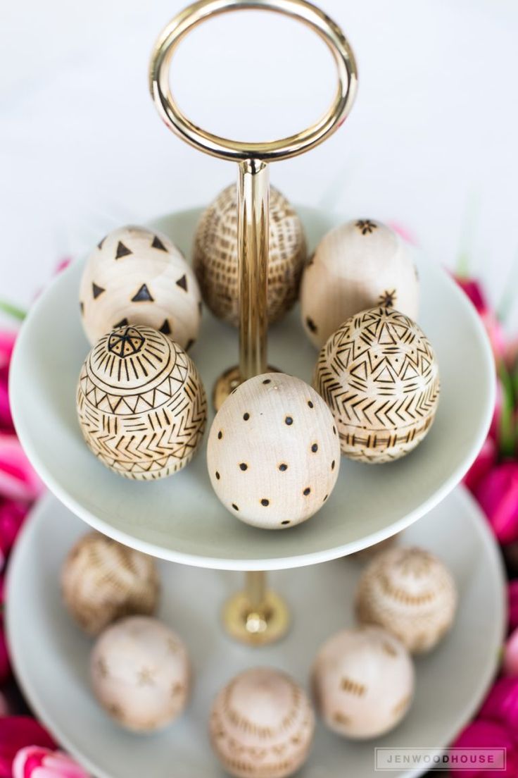 three tiered plate with decorative wooden balls on it and pink flowers in the background