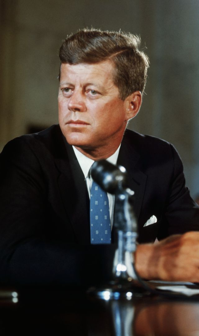 a man in a suit and tie sitting at a table with his hand on the desk