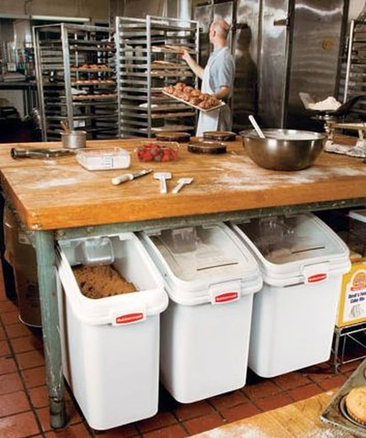 a man in a kitchen preparing food on top of a wooden table with bins