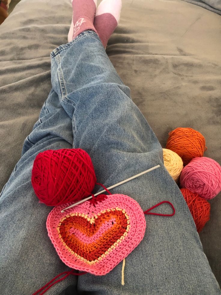 someone is laying on the bed with their feet up and crocheted hearts in front of them