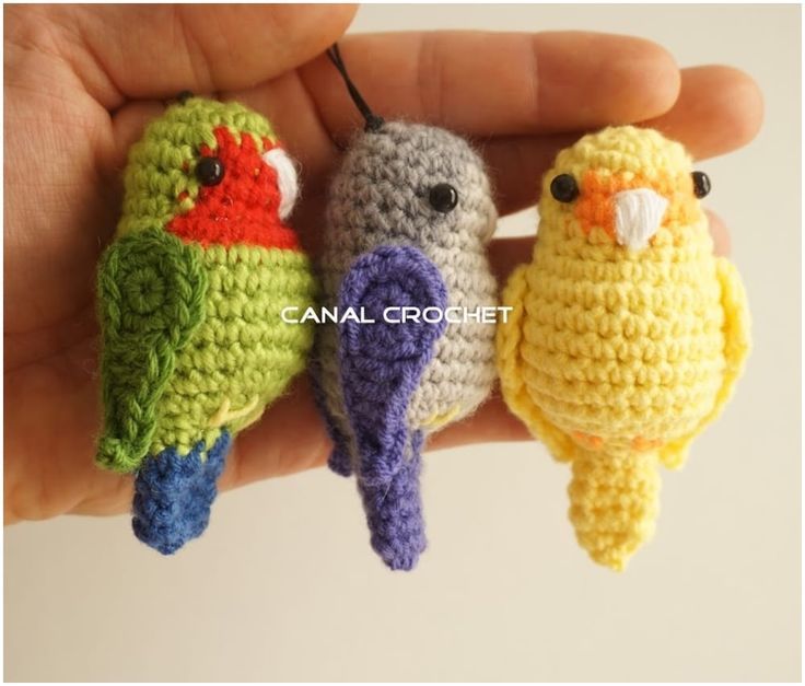 three small crocheted birds sitting on top of each other in front of a person's hand