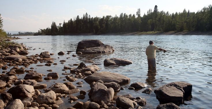 a man standing in the middle of a river next to rocks and holding a fish