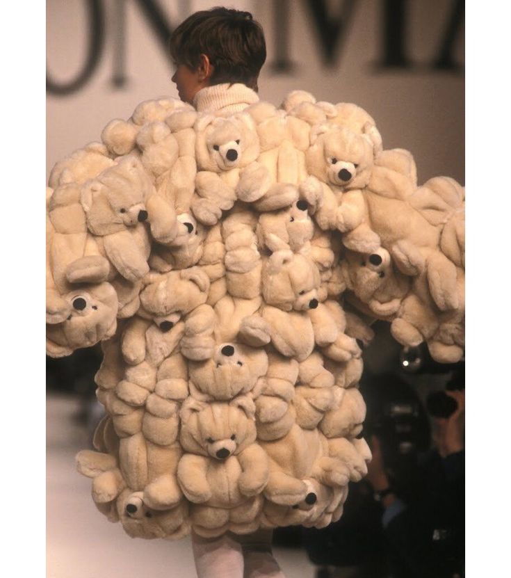 a man is walking down the runway with stuffed animals on his back and arms, all over his body