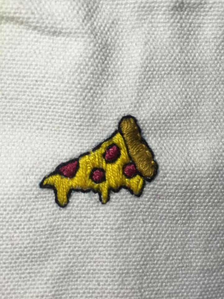 a piece of pizza embroidered on the back of a white shirt with yellow and red dots