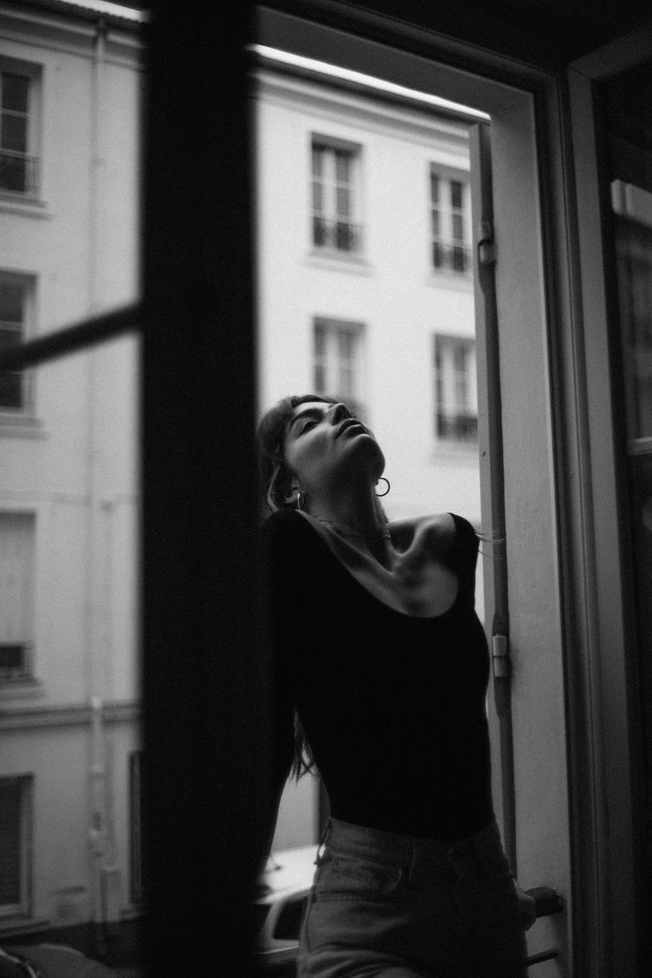 black and white photograph of a woman looking up at the sky from an open window