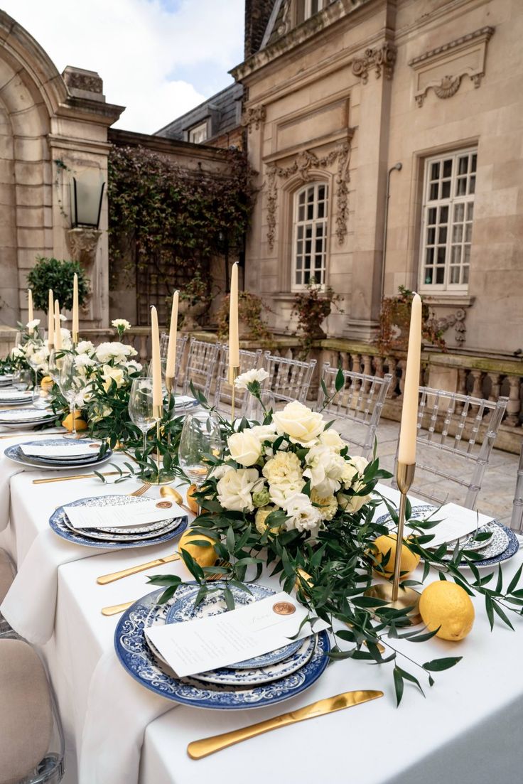 a long table with plates and place settings set up for an outdoor dinner party in front of a large building