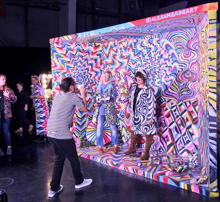 two women standing on a stage in front of a colorful backdrop with people looking at them