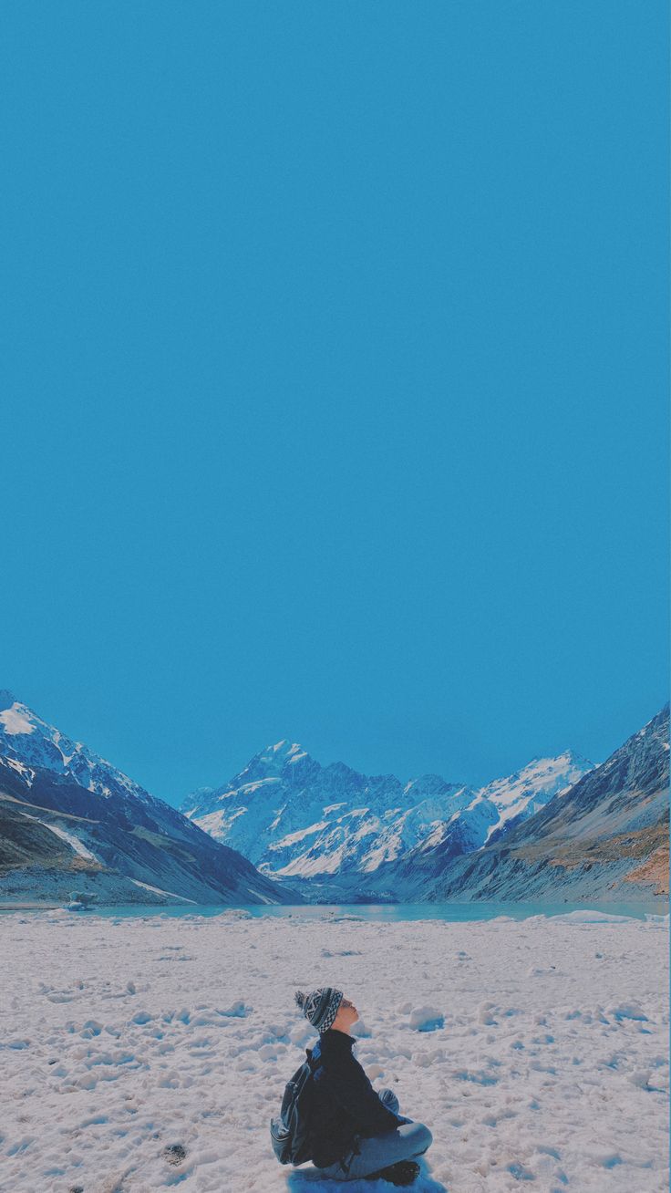 a person sitting in the snow with mountains in the backgroung and blue sky