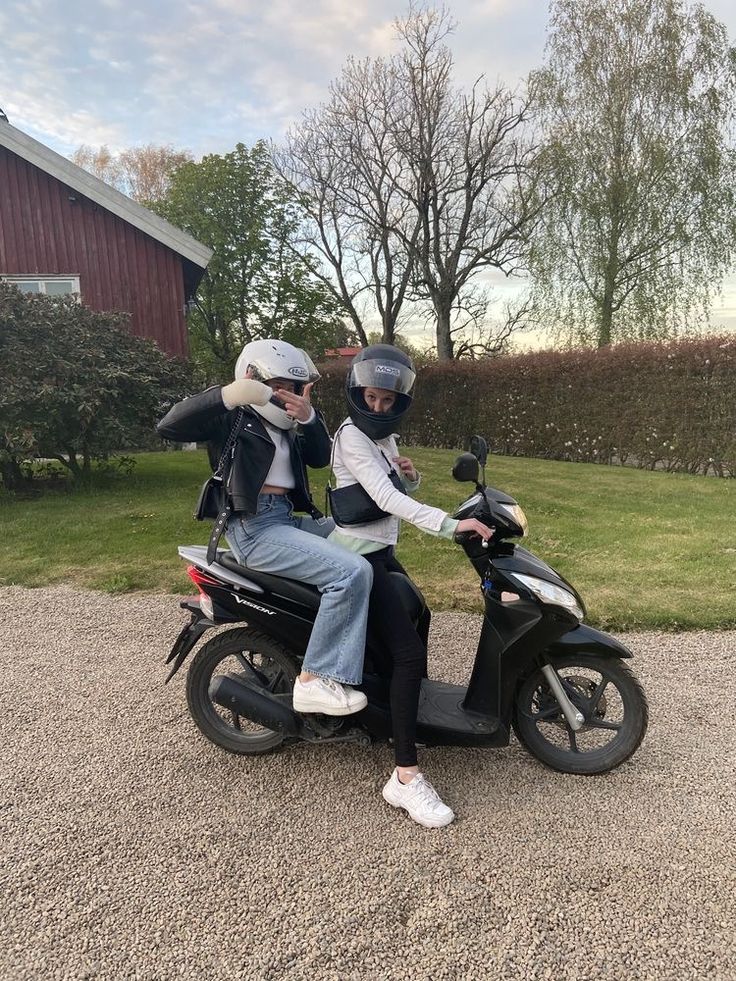 two people sitting on a scooter in front of a barn