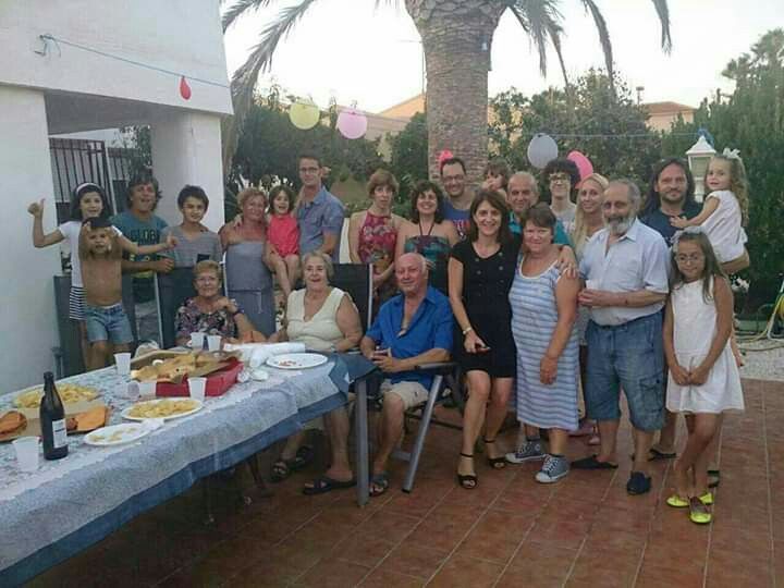 a group of people standing around a table with food and drinks on it in front of a palm tree