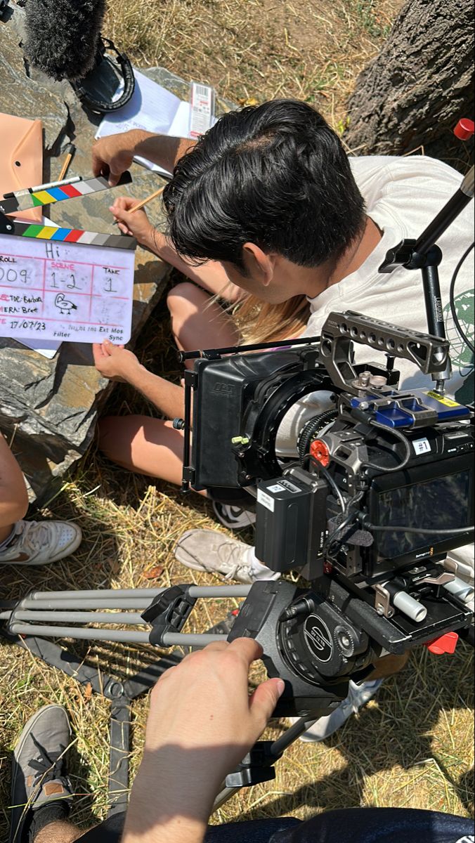 two people sitting on the ground and one person is holding a video camera in front of them