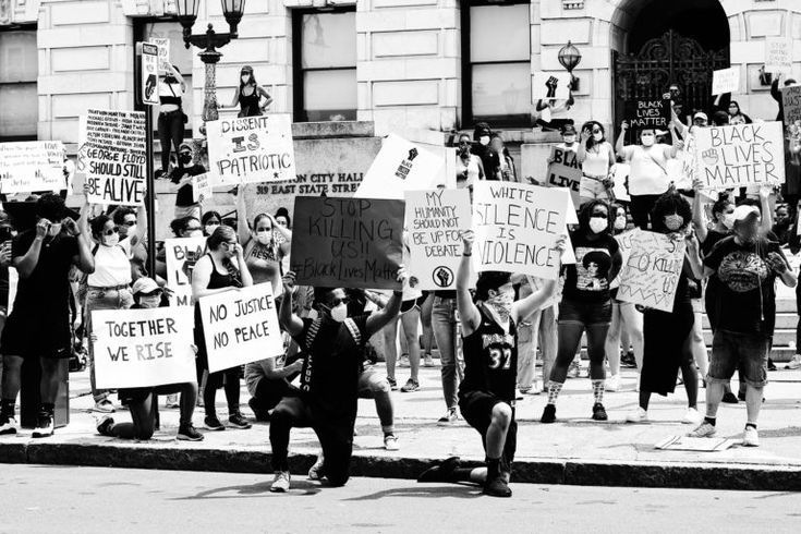 black and white photograph of people protesting in front of a building with protest signs on the street