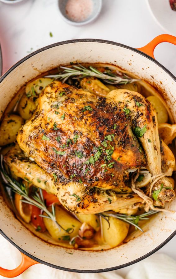 a close up of a chicken in a pot with potatoes and herbs on the side