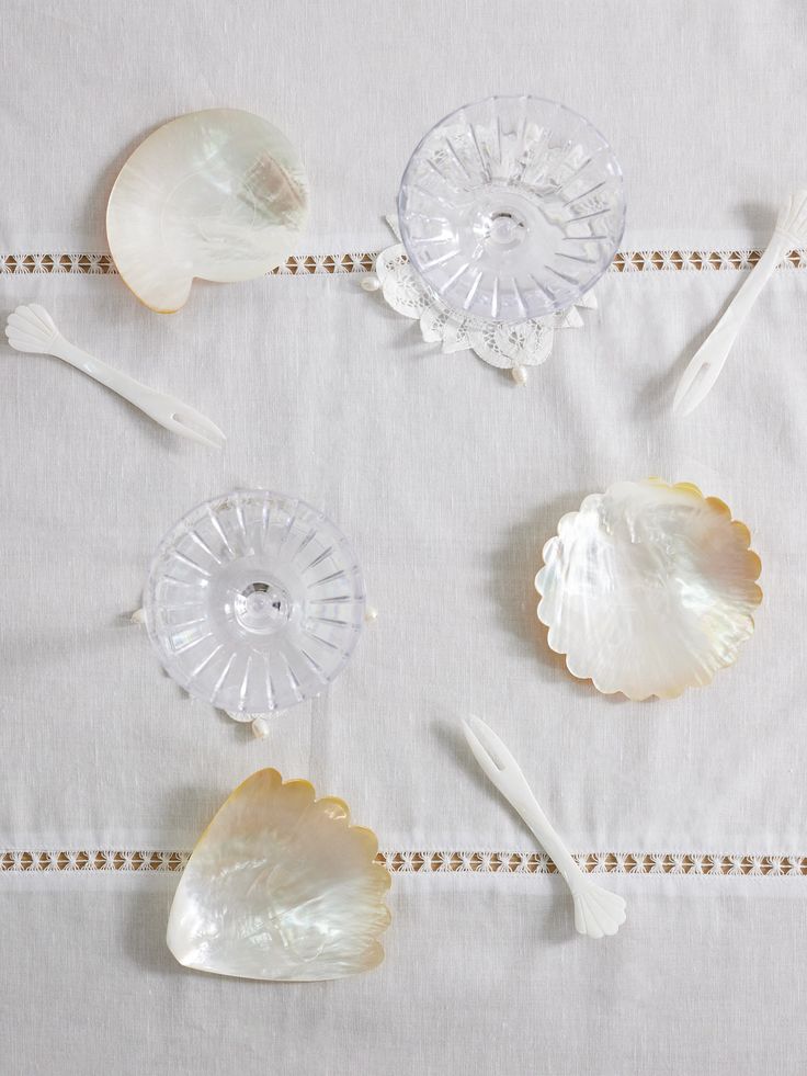 four seashells and spoons on a white tablecloth with beaded border