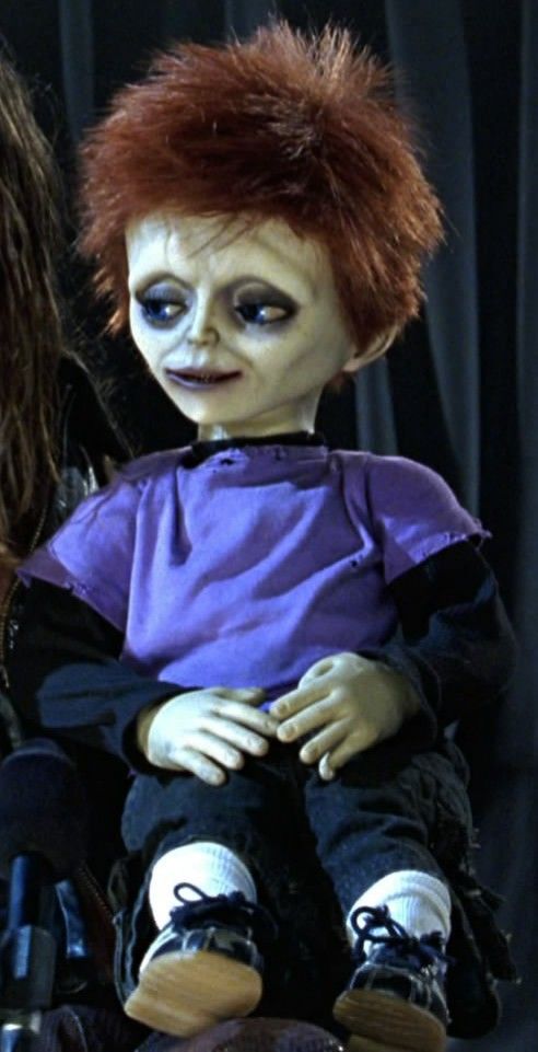 a doll with red hair sitting on top of a woman's lap in front of a black curtain