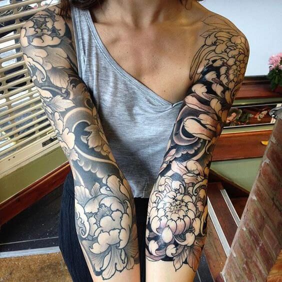 a woman sitting on the floor with her arm covered in flowers and waves tattoo design