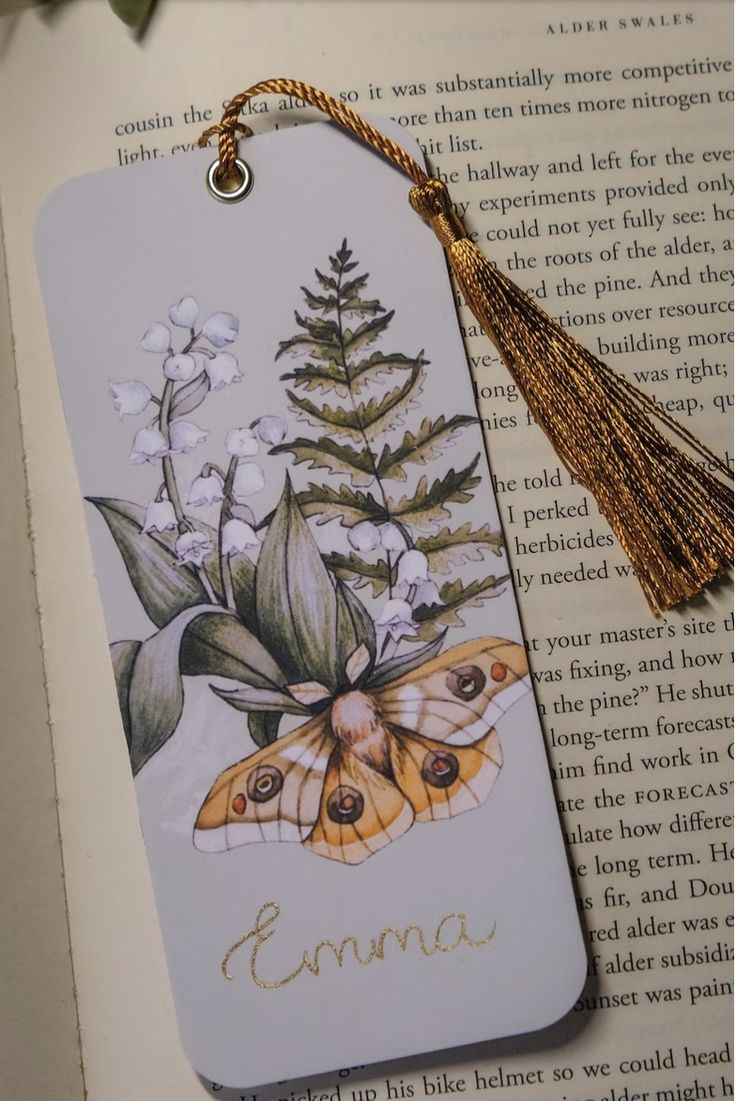 a bookmark with an image of a butterfly and flowers on it, next to a tassel