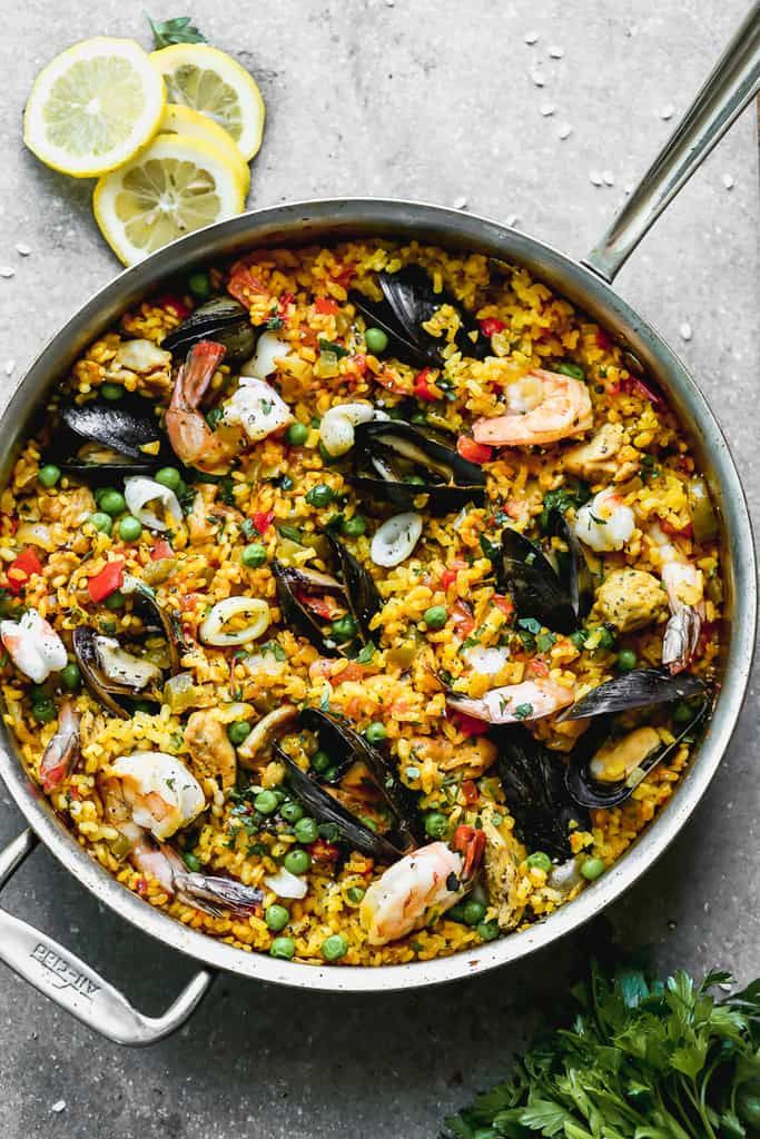 a pan filled with seafood and rice on top of a table next to lemon wedges