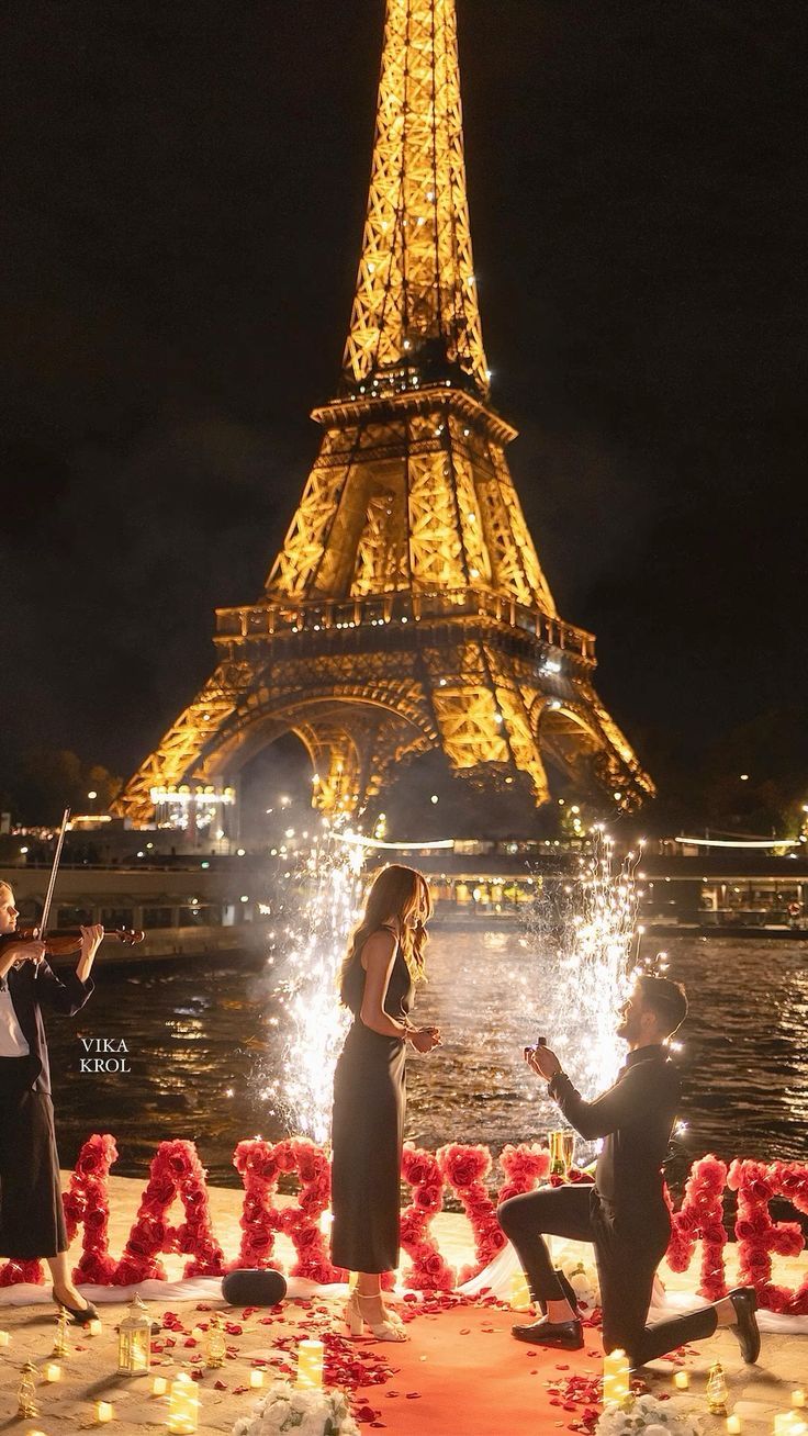 a man kneeling down next to a woman in front of the eiffel tower