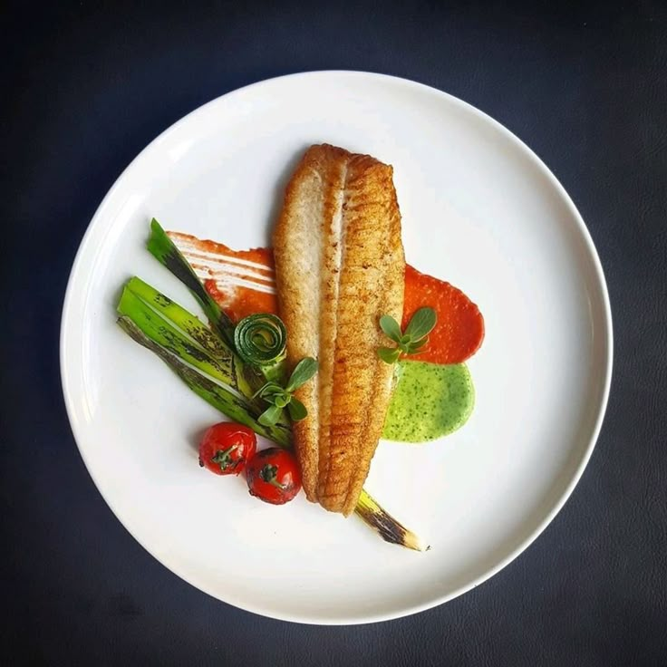 a white plate topped with fish and veggies on top of a black table