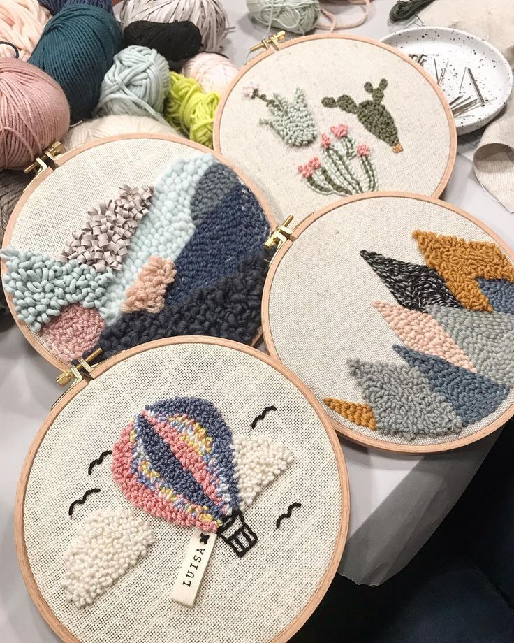 four cross stitch hoops on a table with yarn and crochet work in the background