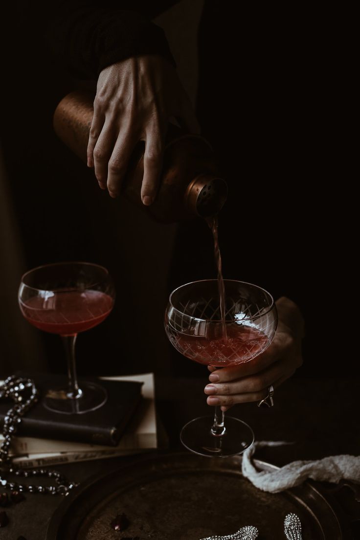 a person pours a drink into two wine glasses