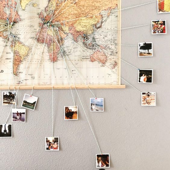 a world map hanging on the wall with many photos attached to it and pinned to strings