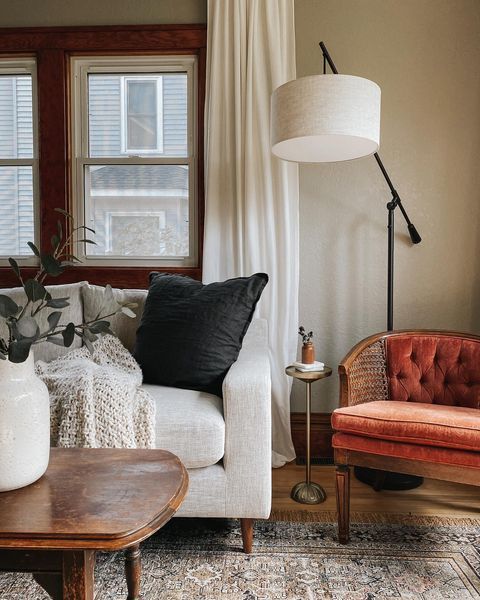 a living room with a couch, chair and table in front of a window that has white curtains