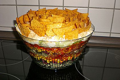 a glass bowl filled with corn chips on top of a black counter next to a white tiled wall