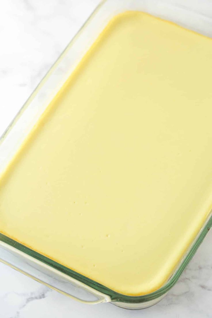 a glass casserole dish filled with yellow liquid on a marble countertop, ready to be cooked